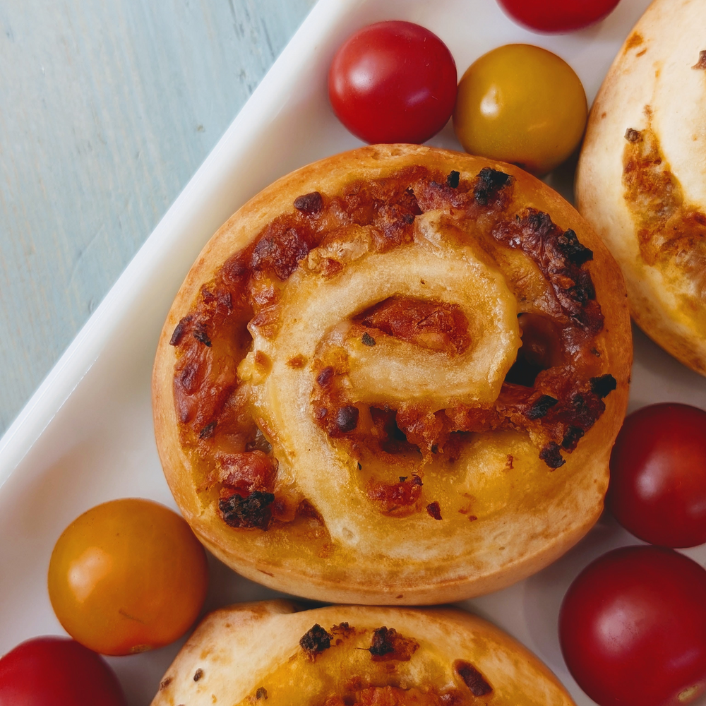Round pizza-roll snacks with melted cheese and tomato bits on a white platter surrounded by red and yellow cherry tomatoes.