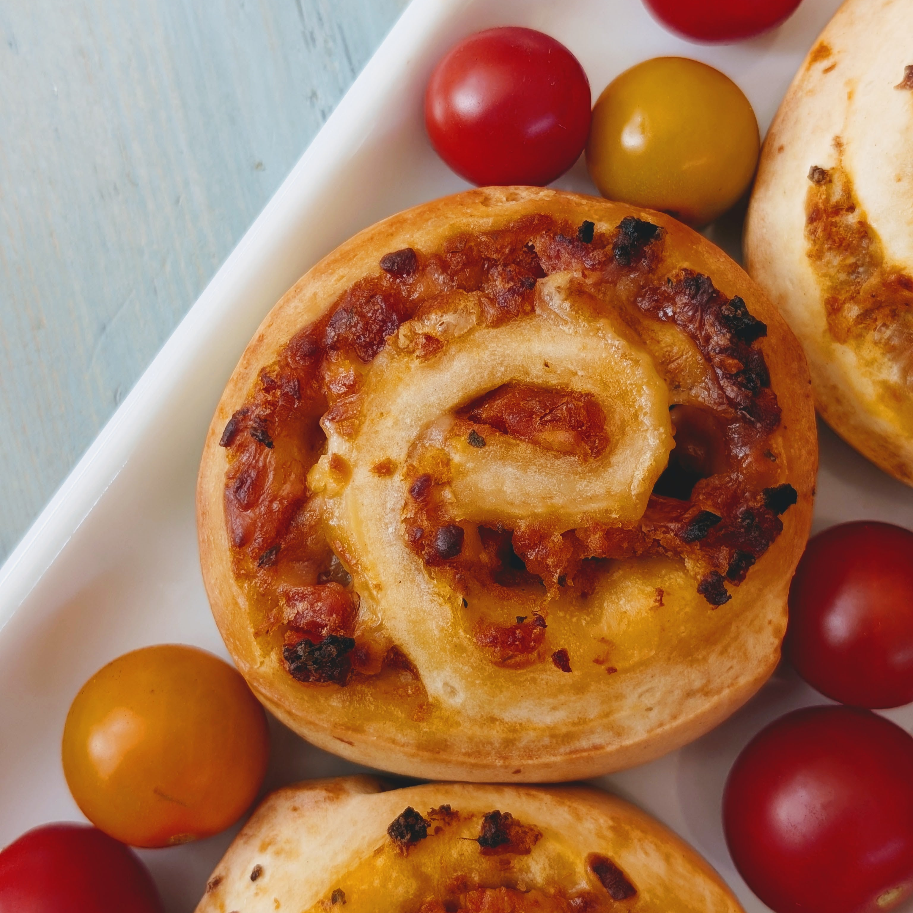 Round pizza-roll snacks with melted cheese and tomato bits on a white platter surrounded by red and yellow cherry tomatoes.