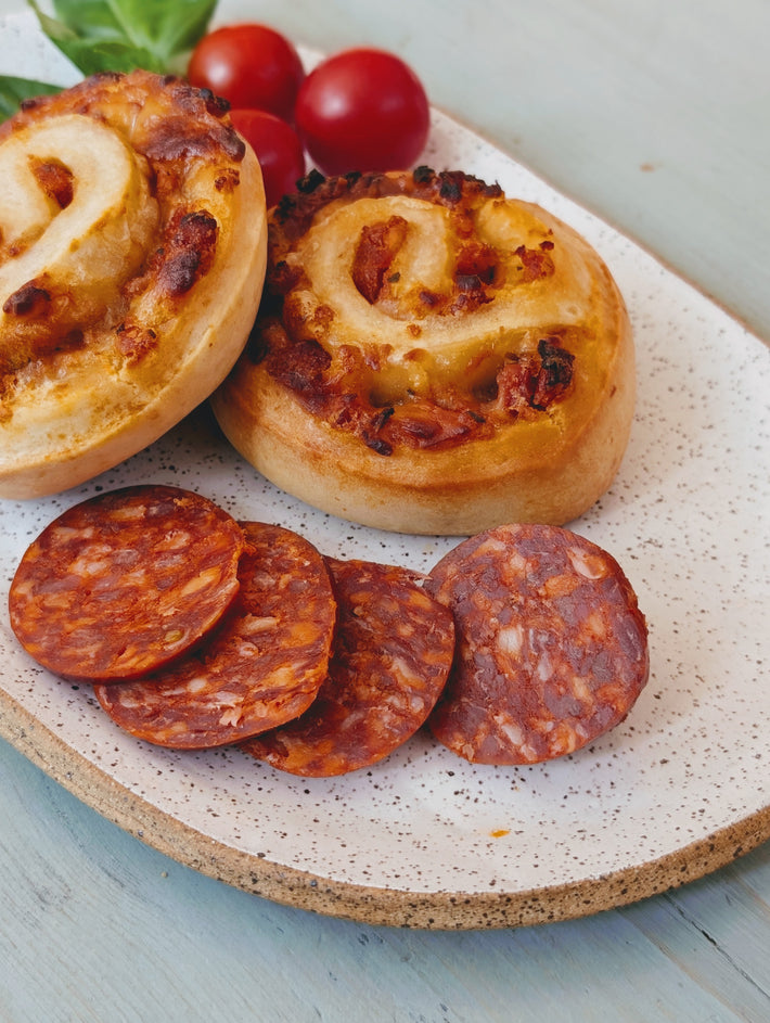 Two savory cheese-and-chorizo pinwheel rolls with sliced chorizo and cherry tomatoes on a speckled ceramic plate