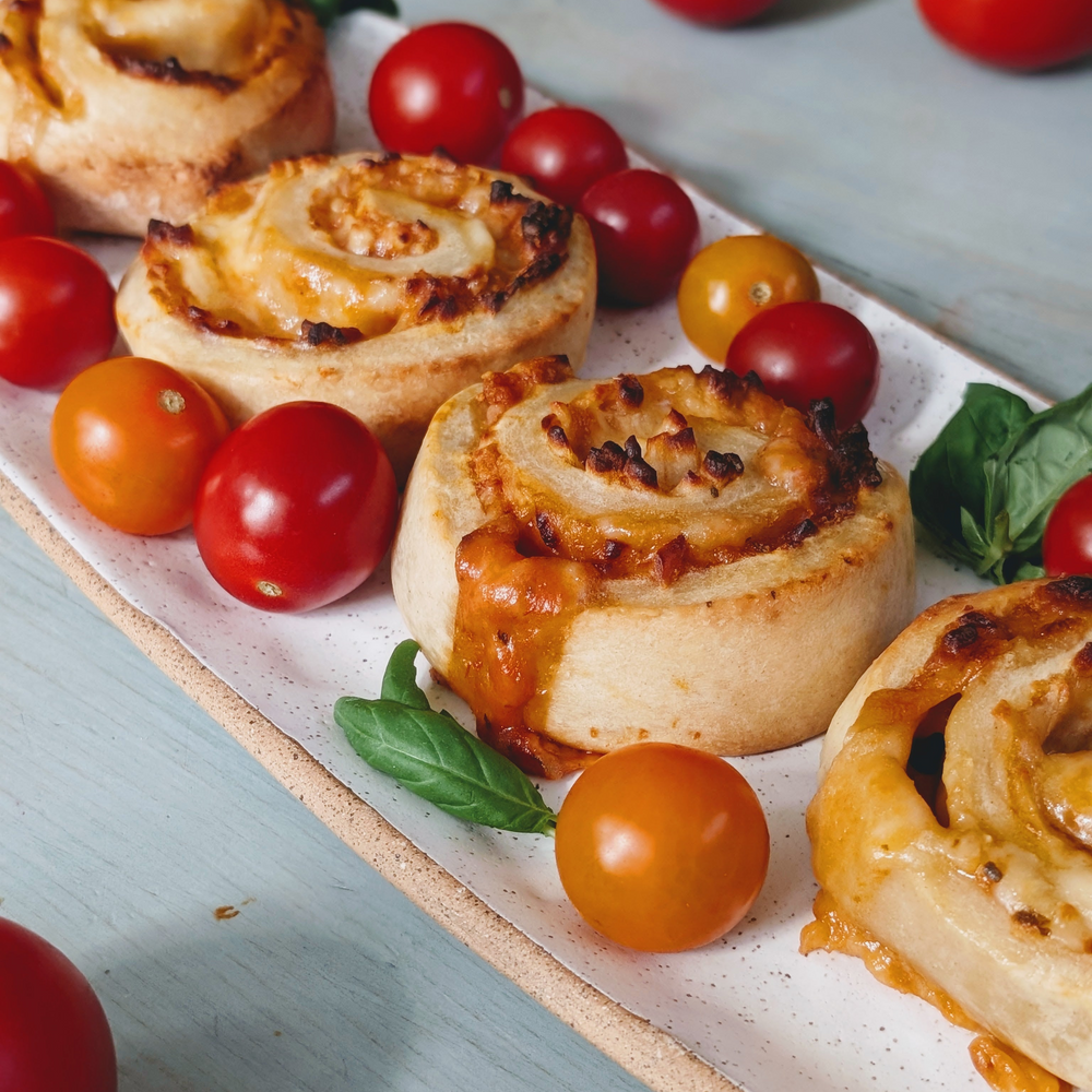 savory cheese pinwheel rolls on a white rectangular platter with cherry tomatoes and basil leaves