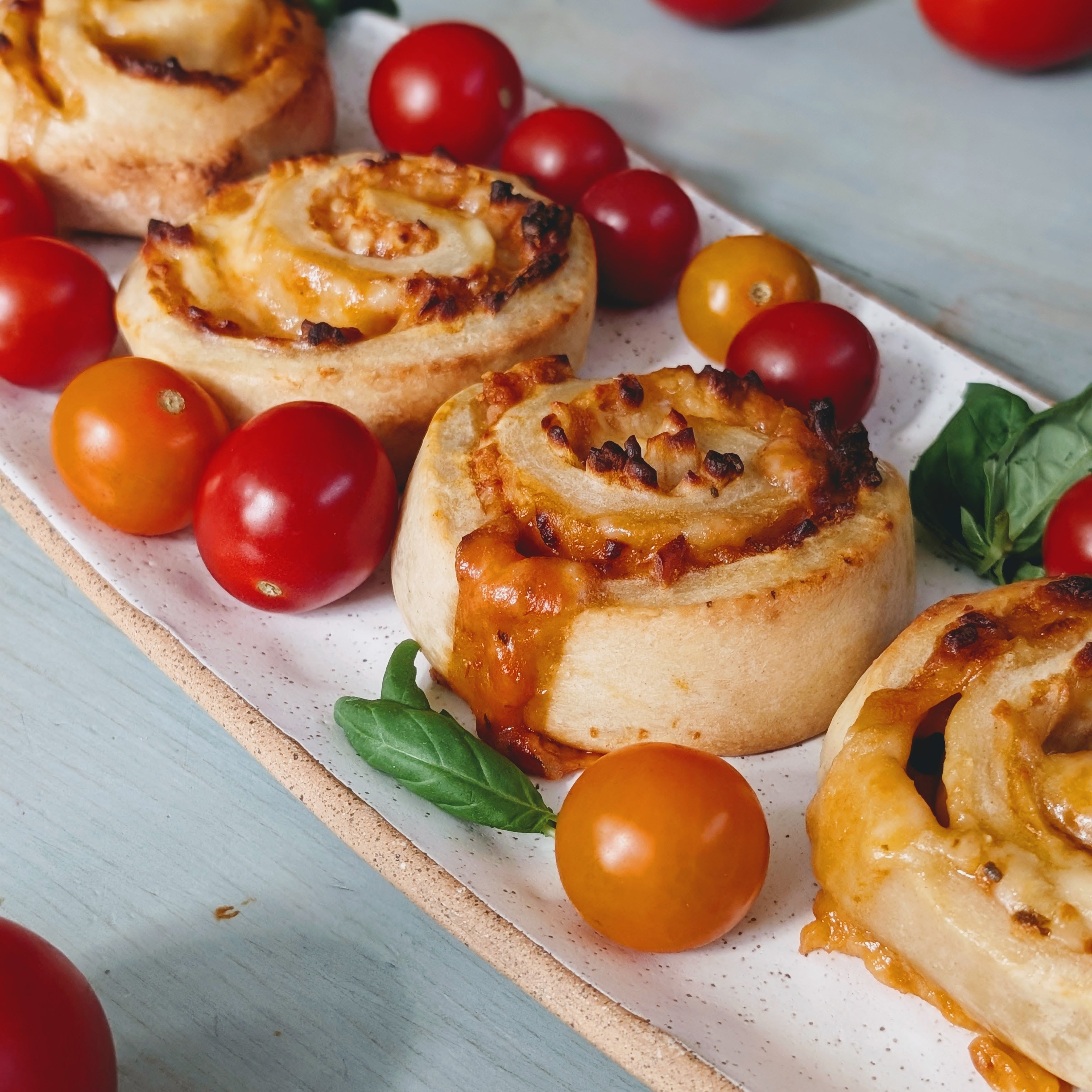 savory cheese pinwheel rolls on a white rectangular platter with cherry tomatoes and basil leaves