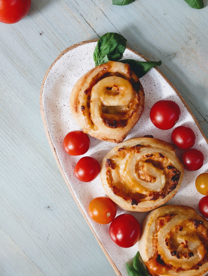 Savory pinwheel rolls with melted cheese on a speckled oval platter with cherry tomatoes and basil.