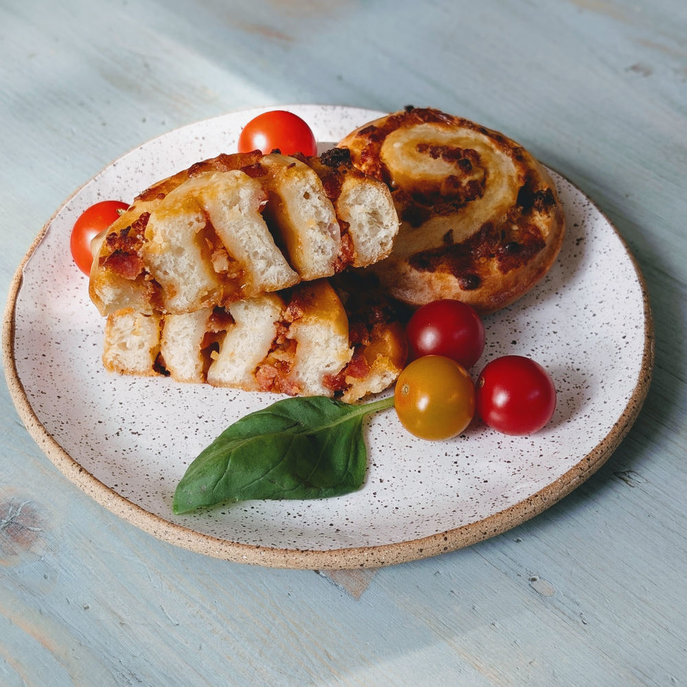 Sliced savory pinwheel pastries with cherry tomatoes and a basil leaf on a speckled white plate