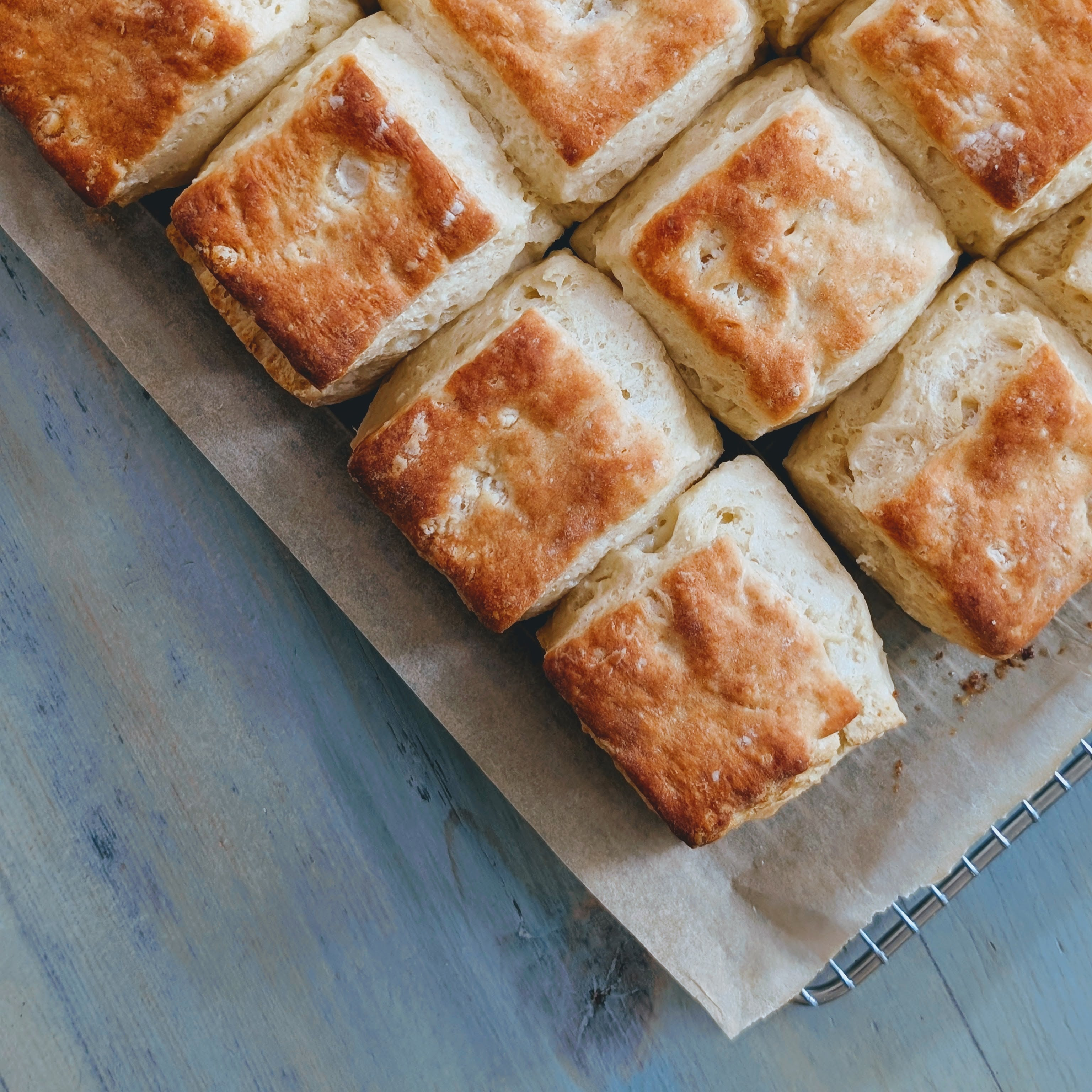 Golden-brown square biscuits arranged on parchment paper and a cooling rack over a blue wooden table