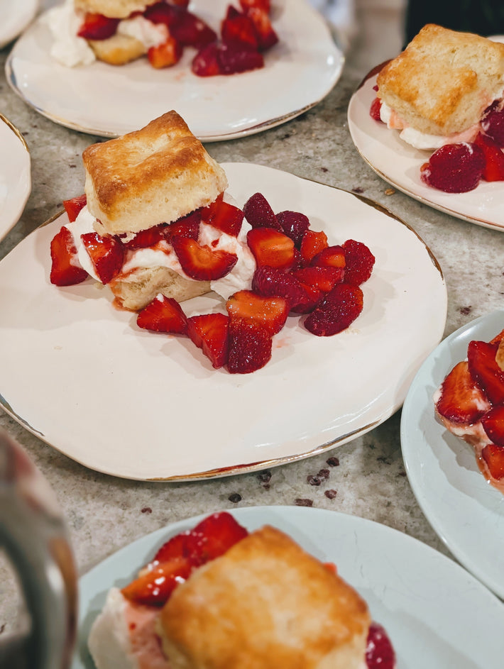 Several biscuit shortcakes with whipped cream and diced strawberries on white plates.