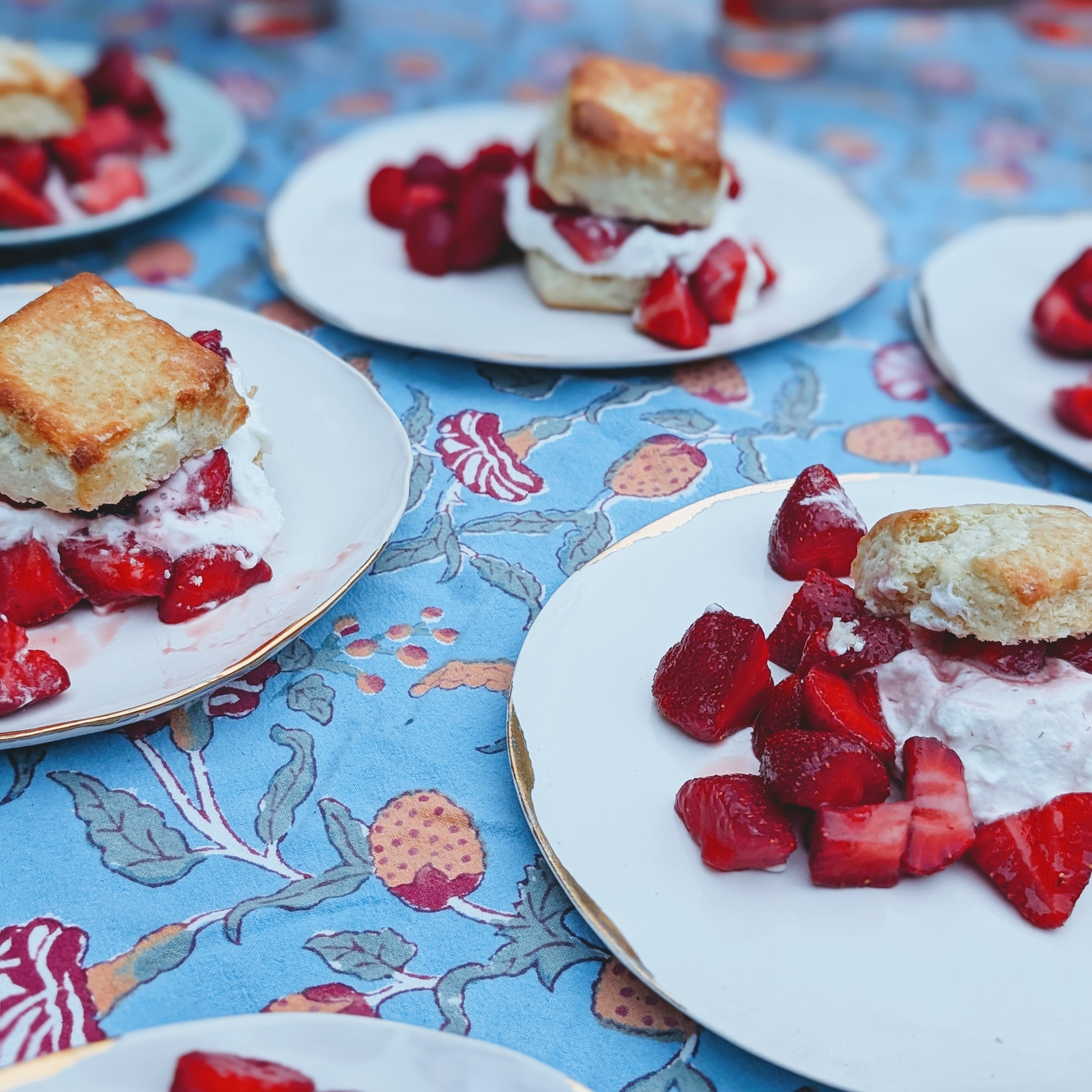 Plates of strawberry shortcakes with whipped cream and diced strawberries on a blue patterned tablecloth