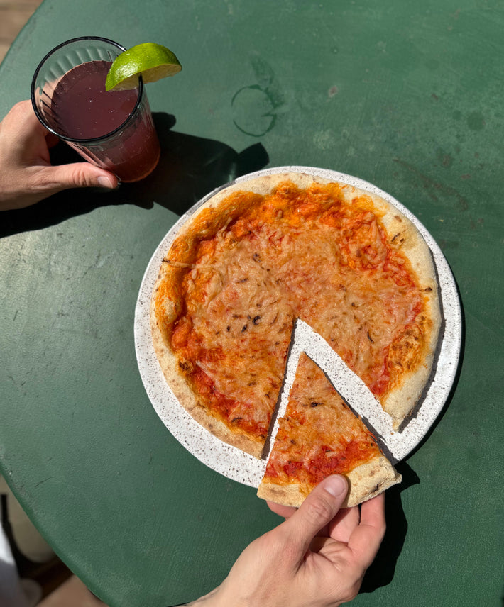 Wildgrain Plant-Based Cheese Pizza on a plate with a drink, slice removed.