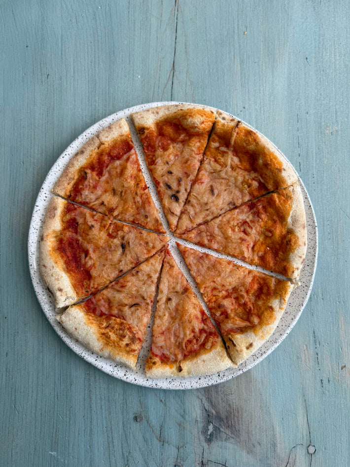 Wildgrain Plant-Based Cheese Pizza with eight slices on a speckled plate.