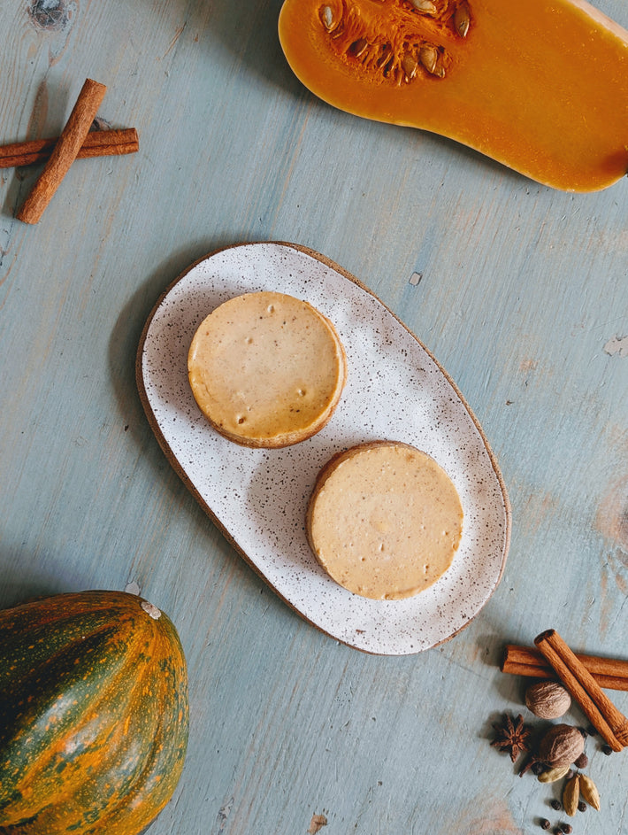Two pumpkin spice cheesecakes on a ceramic plate with pumpkins and cinnamon sticks on a blue surface