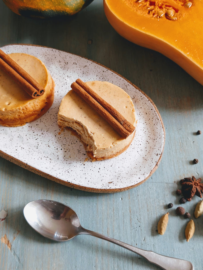 Pumpkin spice dessert on a speckled plate with a spoon and spices on a blue surface
