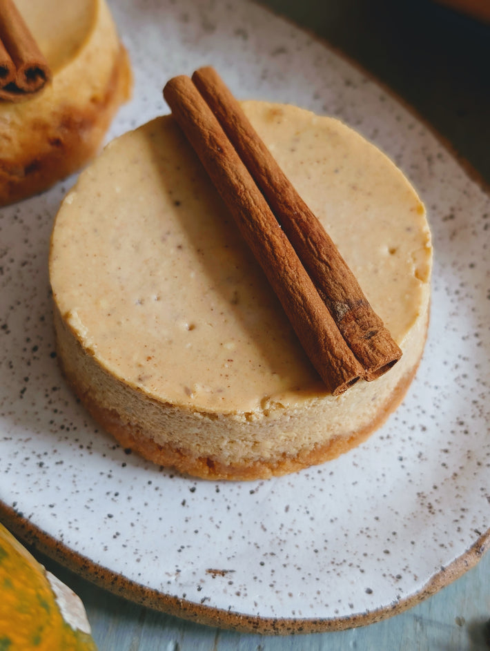 Round cinnamon cheesecake on a speckled ceramic plate topped with two cinnamon sticks