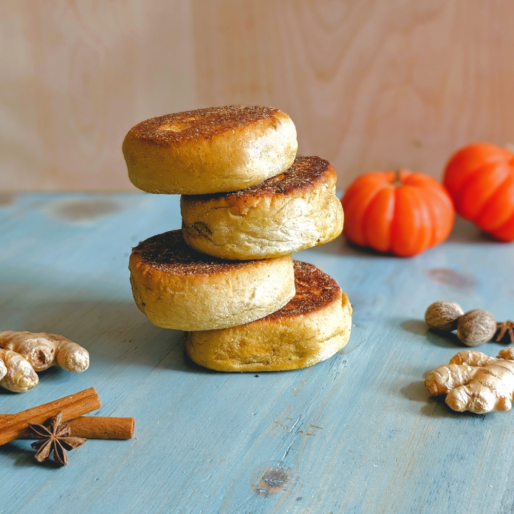 Stack of four toasted English muffins on a blue wooden table with small pumpkins and spices (cinnamon, star anise, ginger).