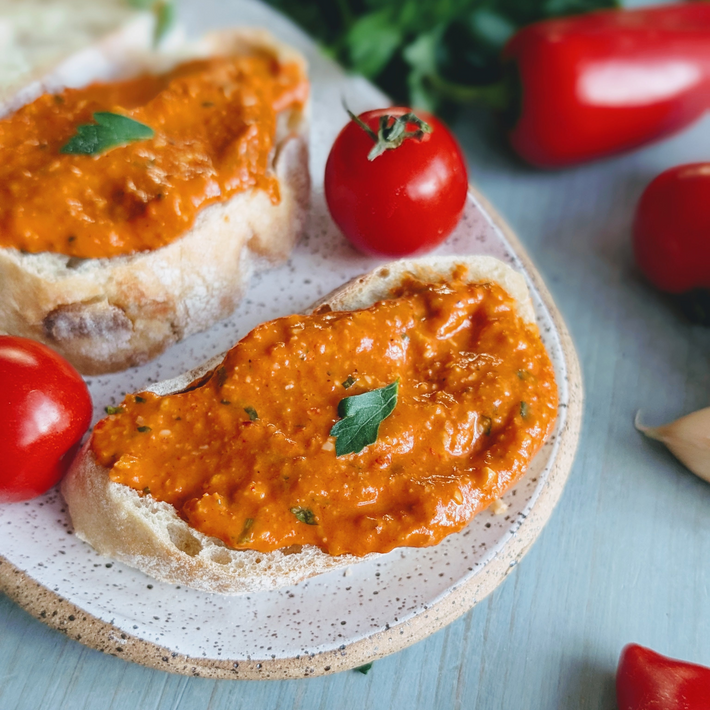 Ciabatta slice topped with red pepper-tomato spread, parsley leaf garnish; cherry tomatoes on speckled plate