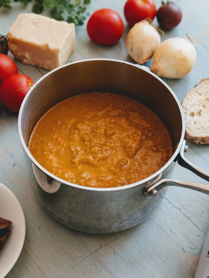 Pot of Wildgrain sauage ragu sauce on a table with vegetables and bread in the background