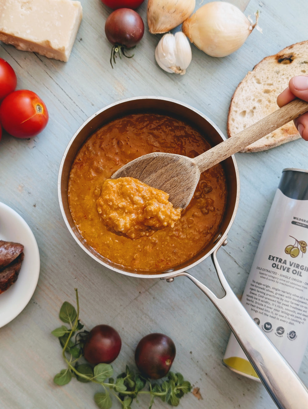 Sausage Ragu Sauce in a pan with a wooden spoon, surrounded by ingredients on a light blue surface.