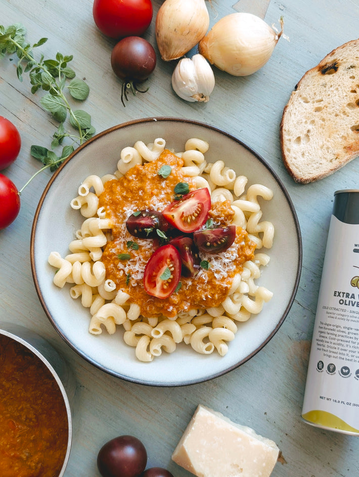 Spiral pasta with tomato sauce, halved cherry tomatoes and herbs; garlic, onions, bread, cheese, and a can labeled EXTRA OLIVE.