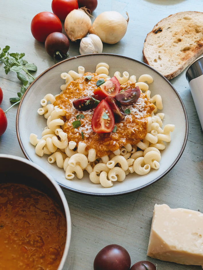 Spiral pasta with tomato-basil meat sauce, grated cheese and halved cherry tomatoes, bread and garlic beside bowl.
