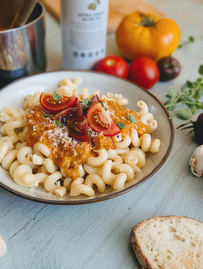 Plate of pasta with tomato sauce and cheese on a wooden table with bread and tomatoes.