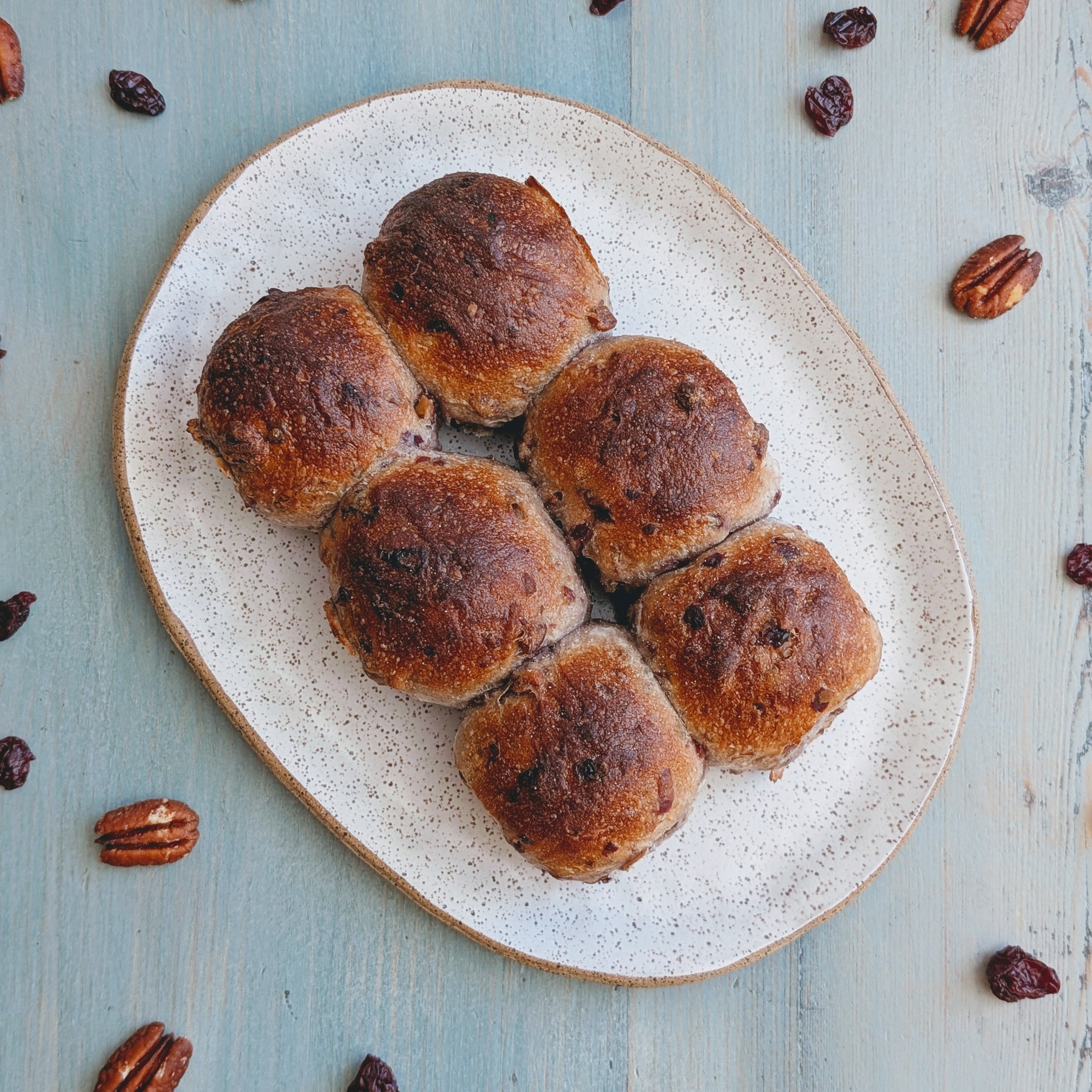 Tear & Share Cranberry-Pecan Rolls on a plate, surrounded by pecans and dried cranberries.