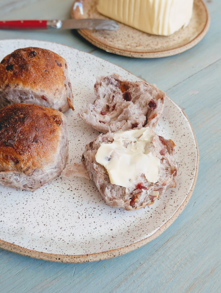 Tear & Share Cranberry-Pecan Rolls on a plate with butter spread on one roll and a butter block in the background.