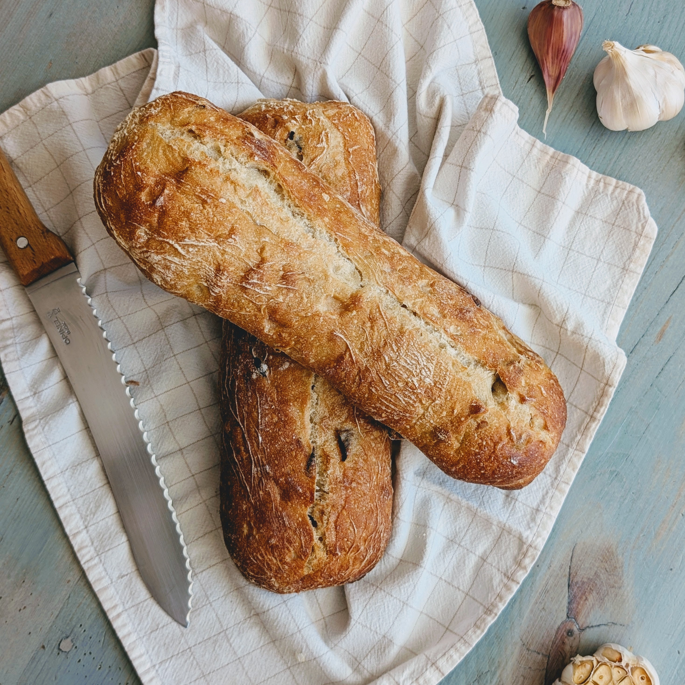 Two Slow-Fermented Garlic Demi Ciabattas on a cloth with garlic and a knife