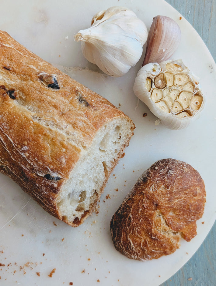 Slow-Fermented Garlic Demi Ciabattas with whole and sliced garlic cloves on a white plate.