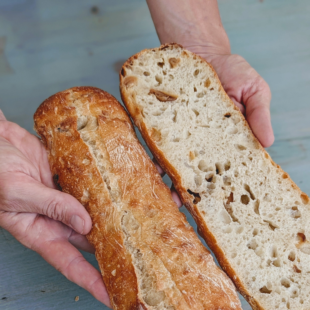 Person's hands holding a halved crusty baguette showing open, airy crumb and golden-brown crust