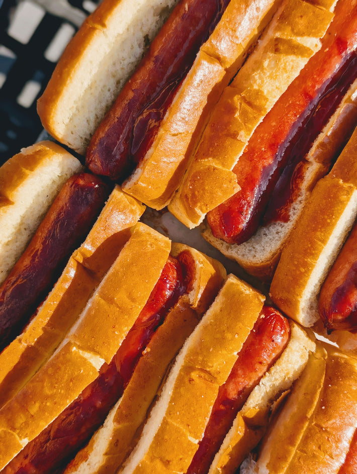 Close-up of grilled hot dogs in soft buns arranged tightly in rows.