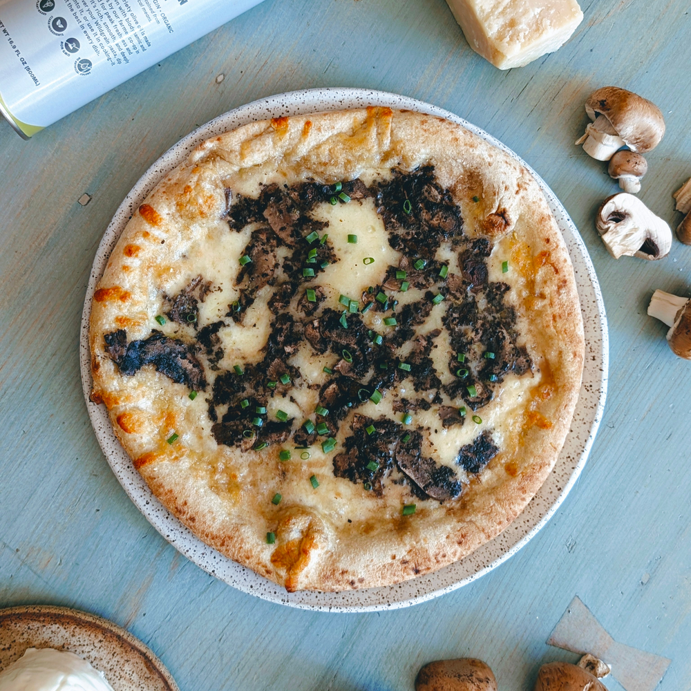 Thin-crust pizza topped with melted cheese, shaved mushrooms, black truffle shavings and chopped chives on a speckled plate