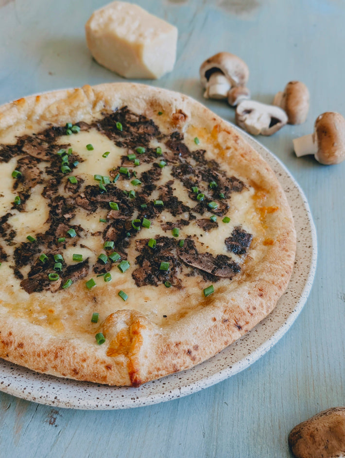 Small pizza with Truffle & mushroom toppings on a speckled plate with mushrooms and cheese in the background.