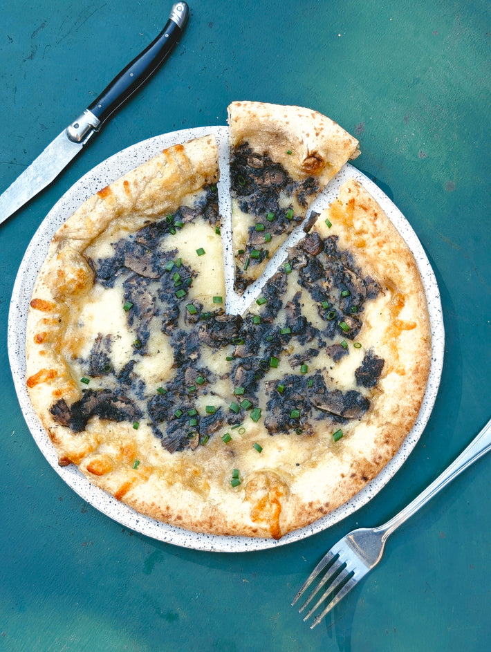 Wood-fired mushroom and melted cheese pizza with chopped chives on a speckled plate, one slice slightly removed.