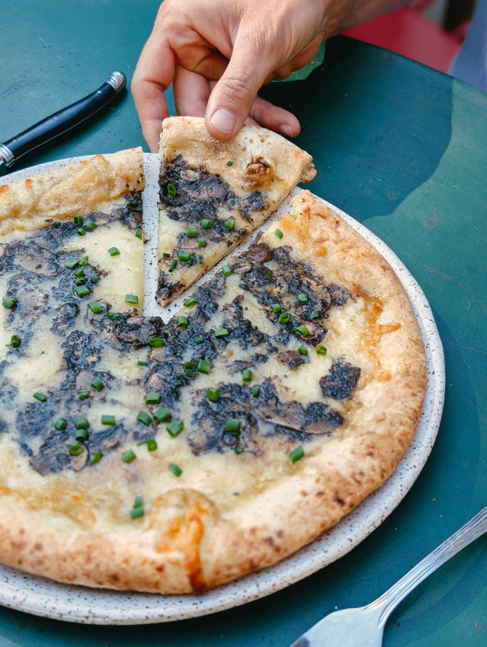 Person taking a slice of Truffle & mushroom and cheese pizza on a green table.