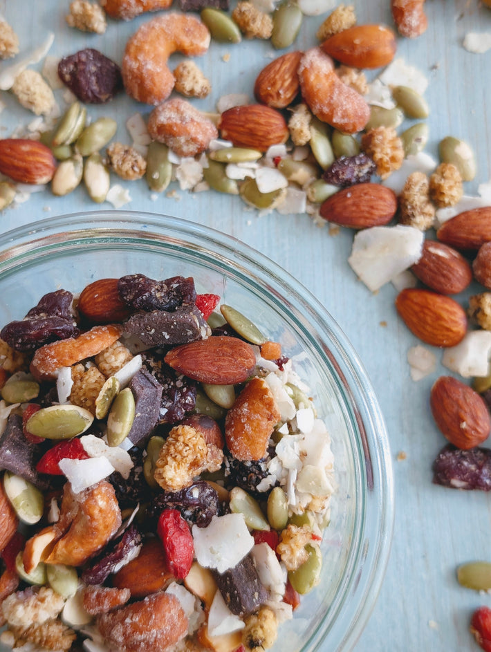 Glass bowl of trail mix with almonds, cashews, pepitas, coconut flakes and dried berries on a blue wooden surface