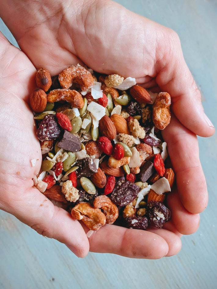 Cupped hands holding mixed trail mix with cashews, almonds, pumpkin seeds, goji berries, coconut flakes and dark chocolate pieces