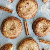 Top-down view of giant snickerdoodle cookies showcasing cinnamon-sugar coating with cinnamon sticks on a painted wooden surface