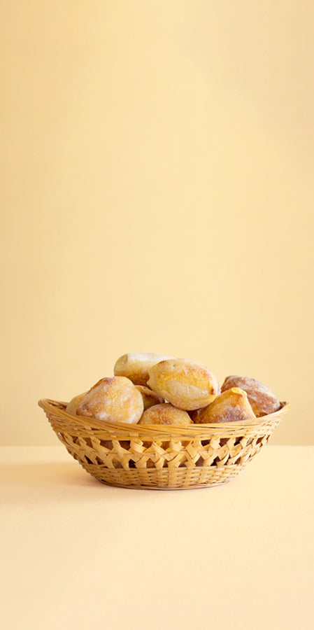 Woven basket filled with small dusted bread rolls on a warm beige background.