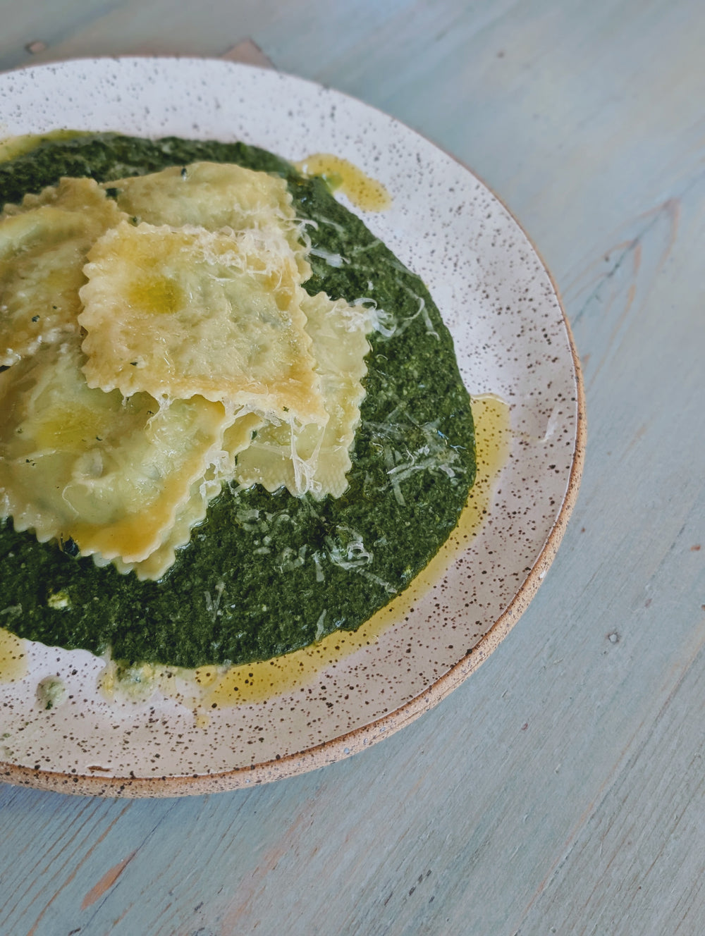 Ravioli on a bed of green sauce with olive oil and cheese