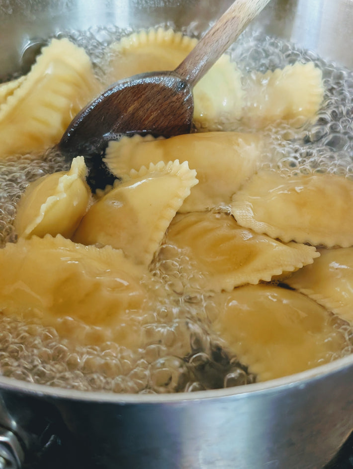 Boiling ravioli in a pot with bubbles and a wooden spoon stirring.
