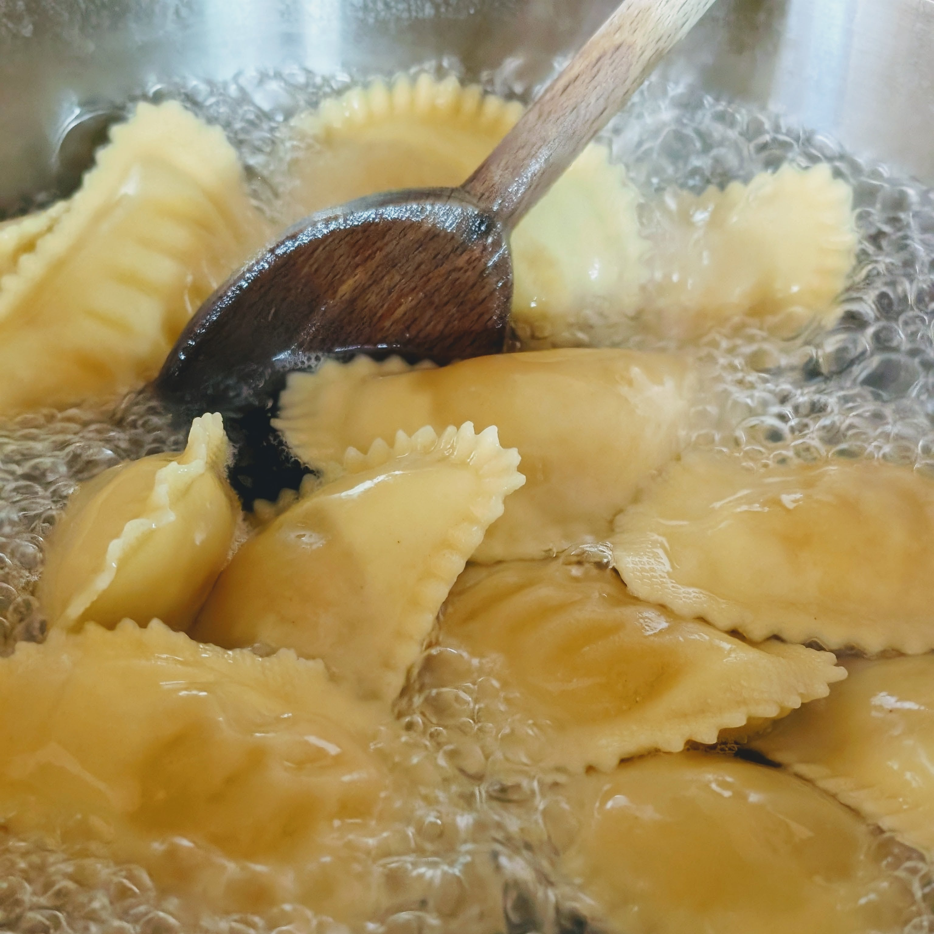 Ravioli boiling in a pot being stirred with a wooden spoon
