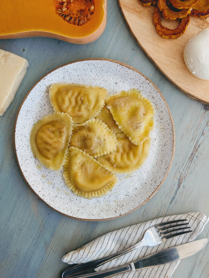 Butternut Squash & Cheese Ravioli on a plate with cheese and cutlery.