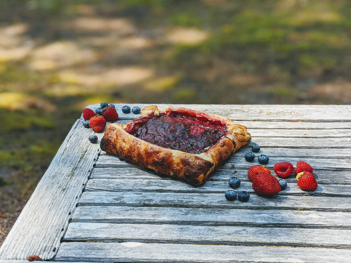 Triple Berry Galette on a wooden table with strawberries, blueberries, and raspberries.