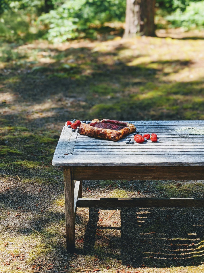 Triple Berry Galette on a rustic wooden table with strawberries in a forest setting.