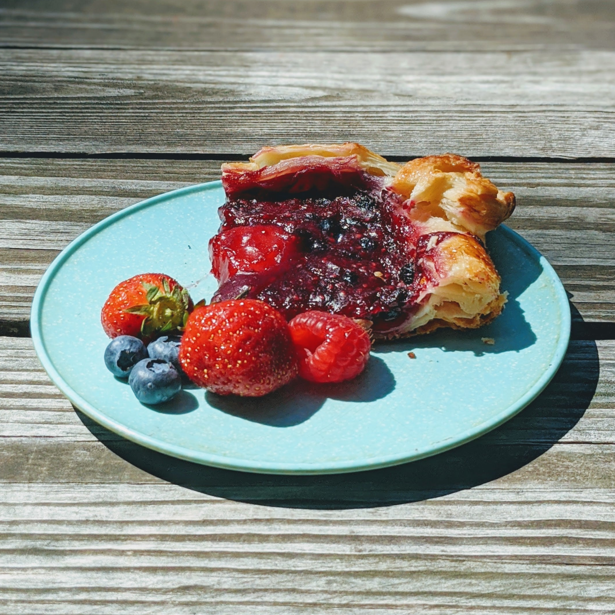 Mixed-berry galette slice with strawberries, raspberries, blueberries on a blue plate on a weathered wooden table