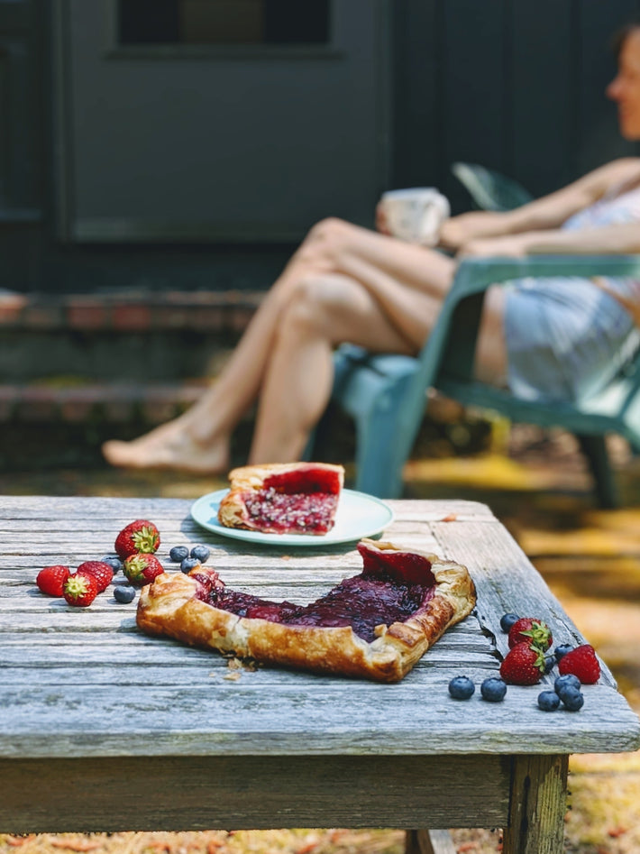 A slice of Triple Berry Galette on a rustic table with fresh strawberries and blueberries.