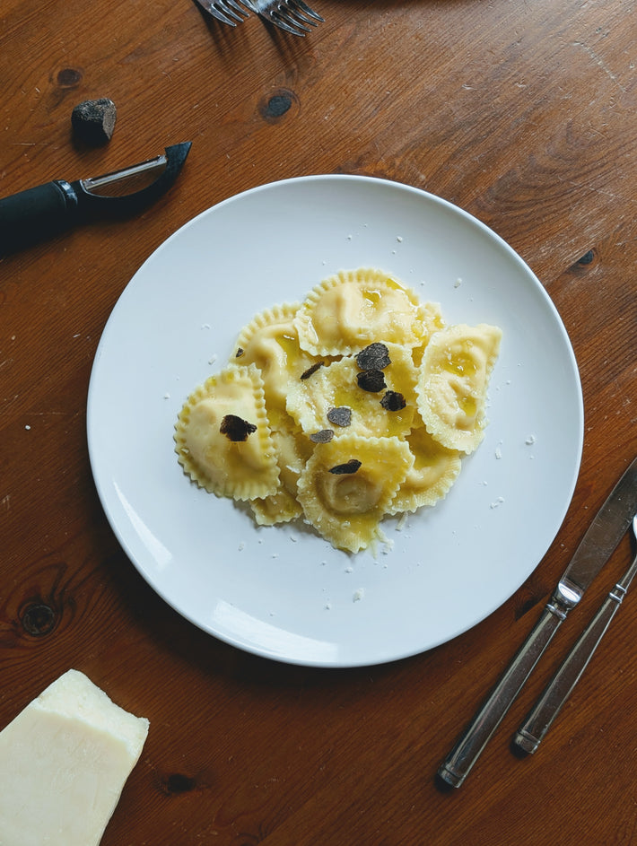 Truffle ravioli topped with black truffle slices and grated cheese on a wooden table.