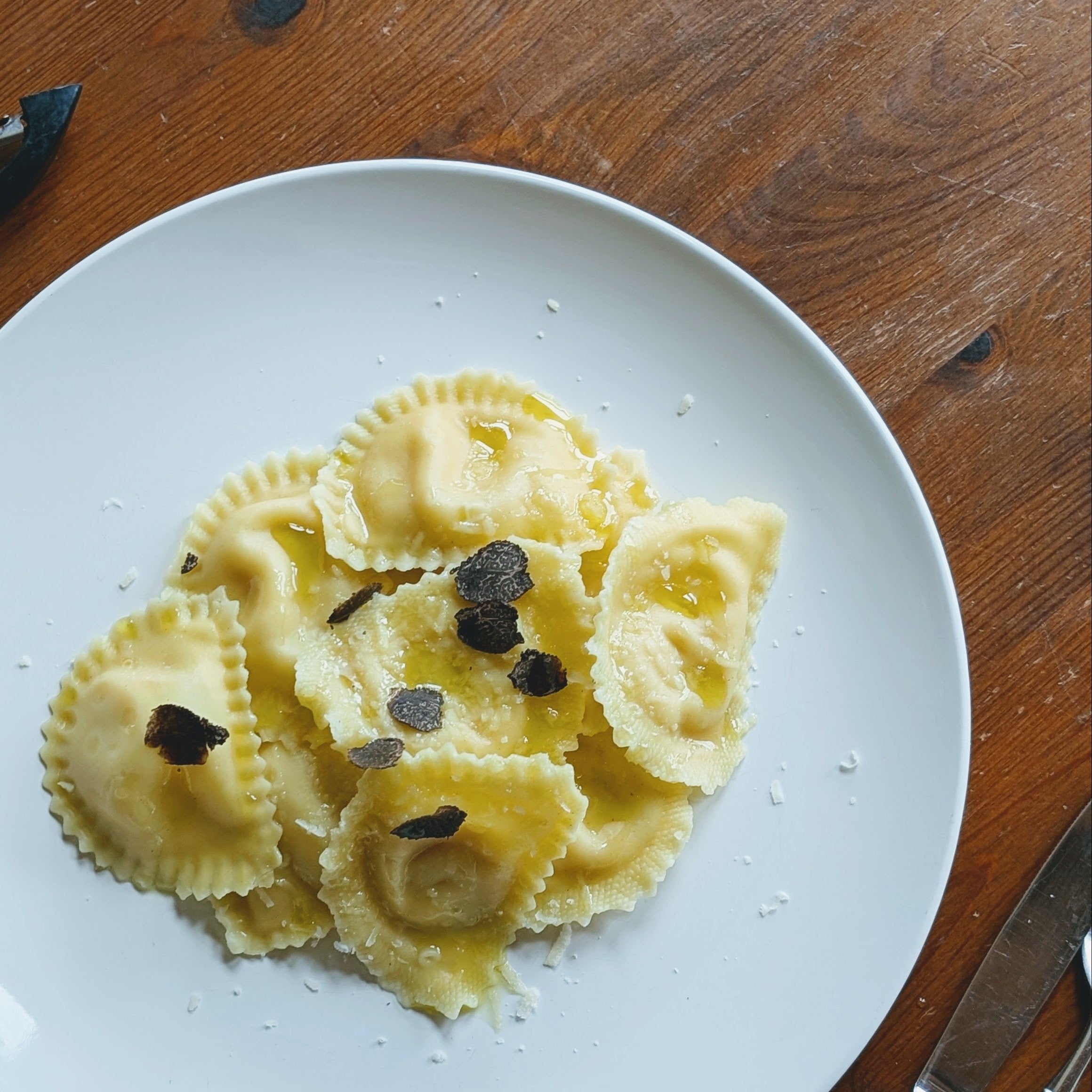 Plate of ravioli pasta topped with shaved black truffles and grated cheese on a wooden table.