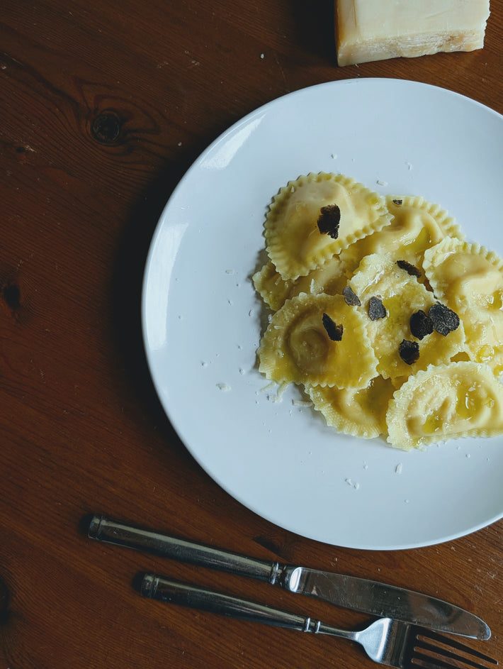 Truffle & Parmigiano Reggiano Ravioli on a plate with black truffle shavings, served with cutlery.