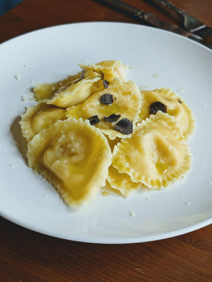 Truffle & Parmigiano Reggiano Ravioli on a plate, topped with black truffle shavings and cheese.