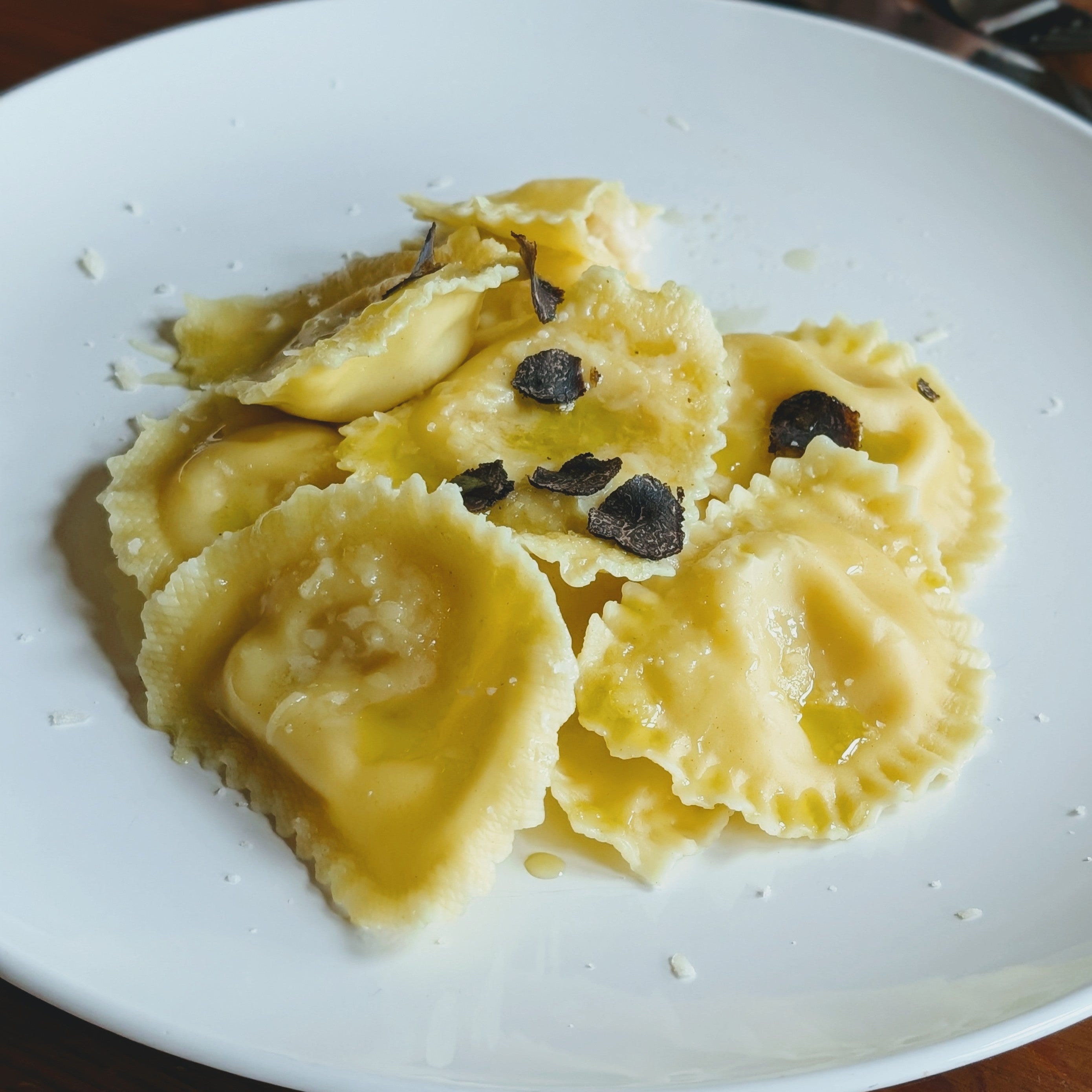 Plate of buttered ravioli topped with shaved black truffle and grated cheese.
