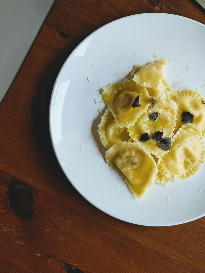 Truffle & Parmigiano Reggiano Ravioli on a white plate, some topped with black truffle pieces.